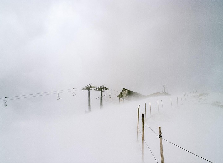 A ski lift and building are barely visible through heavy fog and snow on a mountain.