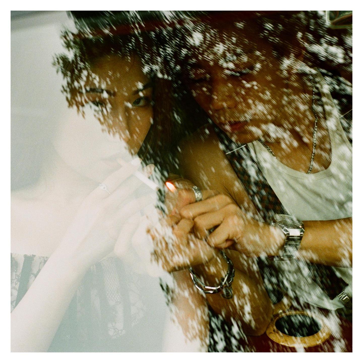 A person lights a cigarette, with reflections of foliage visible on the surface.