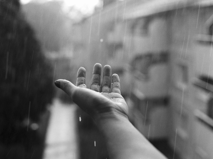 A hand is held out to catch raindrops in a black and white photograph.