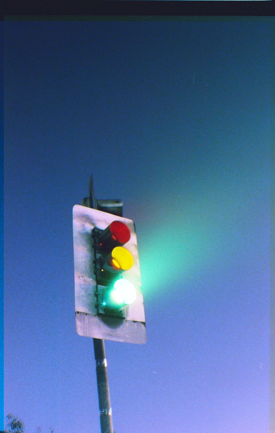 A traffic light with a green light illuminated is captured against a blue sky.