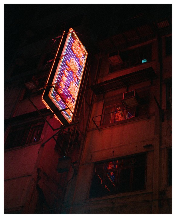A neon sign with orange and purple lights is mounted on the side of a building at night.