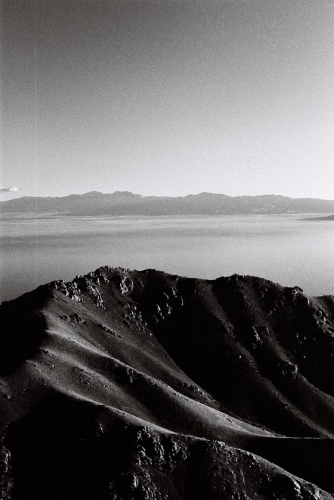 A mountain ridge casts a shadow over a lake with distant mountains under a clear sky.