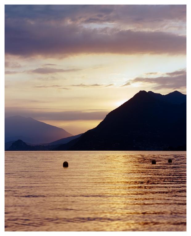 The sun rises over a lake with mountains in the background and buoys in the water.