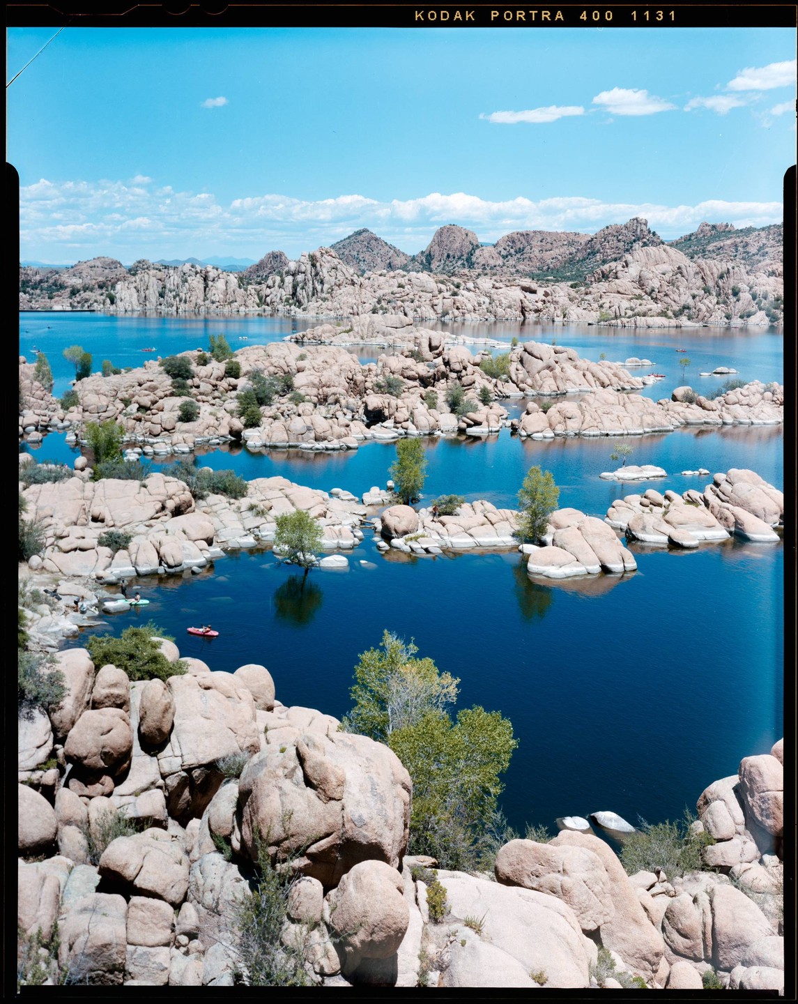 A large body of water is surrounded by many small, rocky islands and mountains under a blue sky.