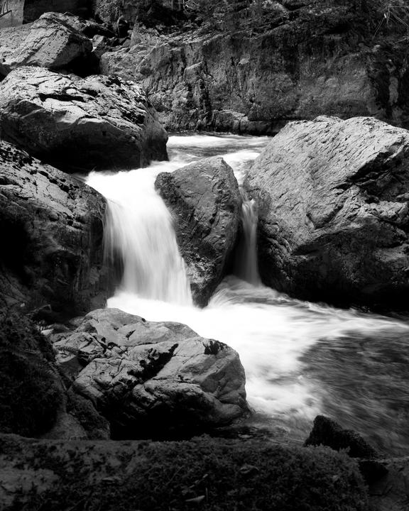 A river flows over and around large rocks, creating small waterfalls and rapids.