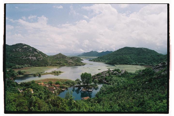A wide shot shows a lake surrounded by mountains and a small village with houses and boats.