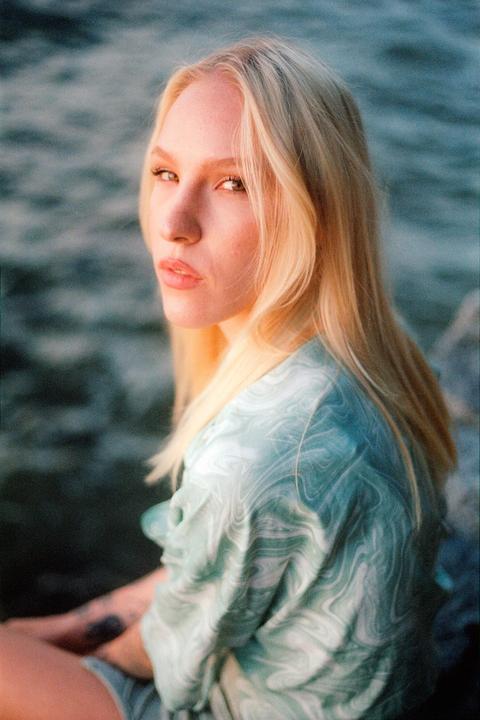 A woman with long blonde hair and a patterned shirt looks over her shoulder at the viewer.