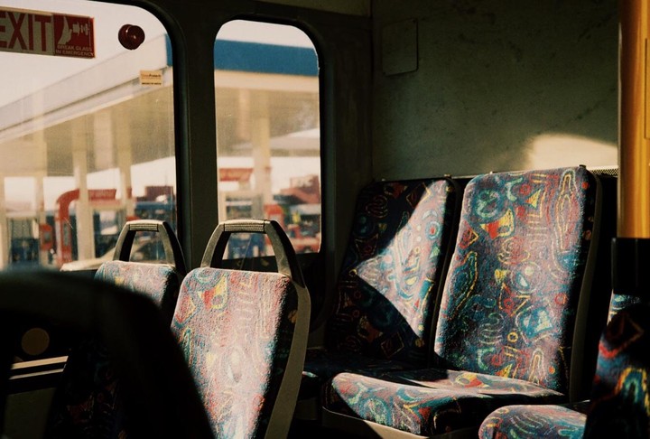 Sunlight streams through the window of a bus, illuminating the patterned seats.