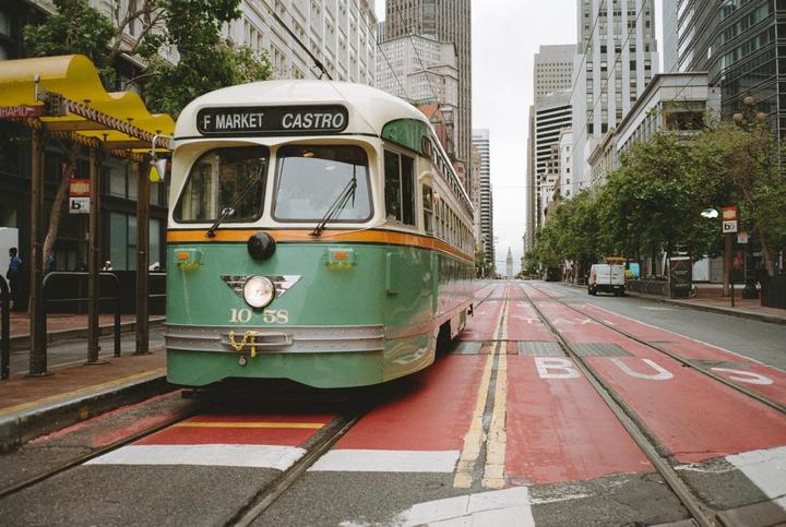 A green and orange streetcar is parked on a street with red bus lanes and tall buildings in the background.