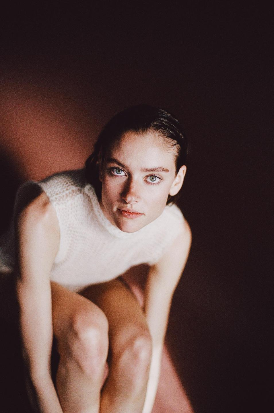 A woman with wet hair and a white top looks up at the viewer.