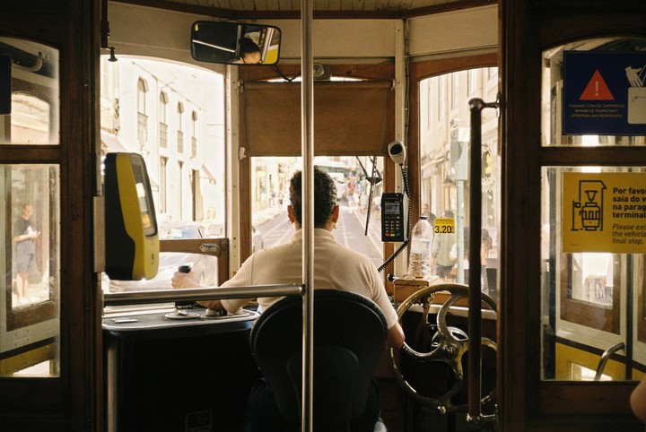 A tram driver is visible from behind, operating the vehicle on a city street.