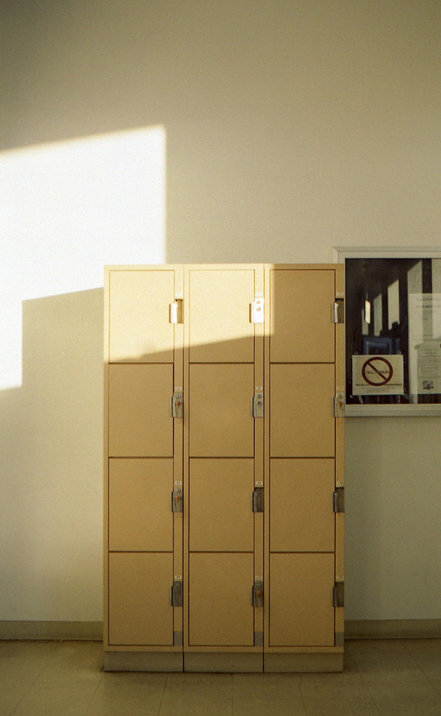 A bank of lockers stands against a wall with a window and a sunlit shadow.
