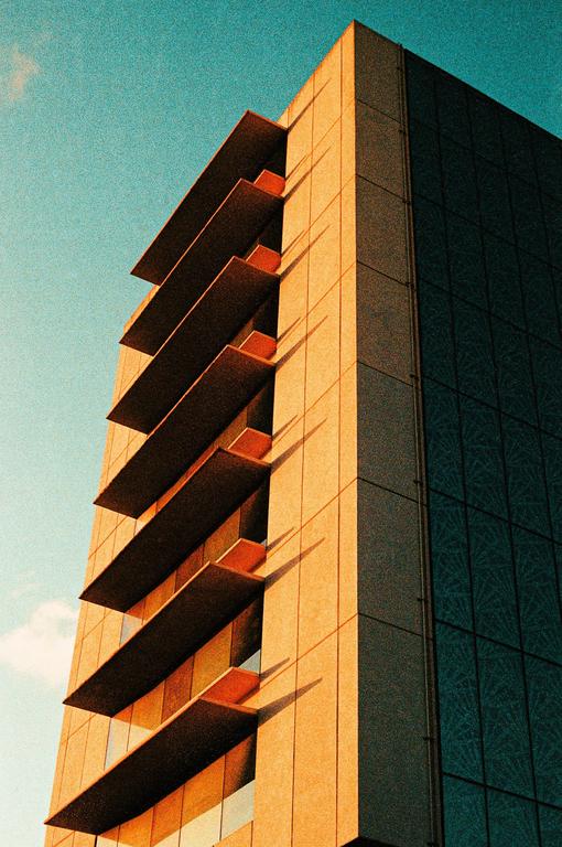 A tall building with a textured facade and dark windows is illuminated by sunlight against a blue sky.