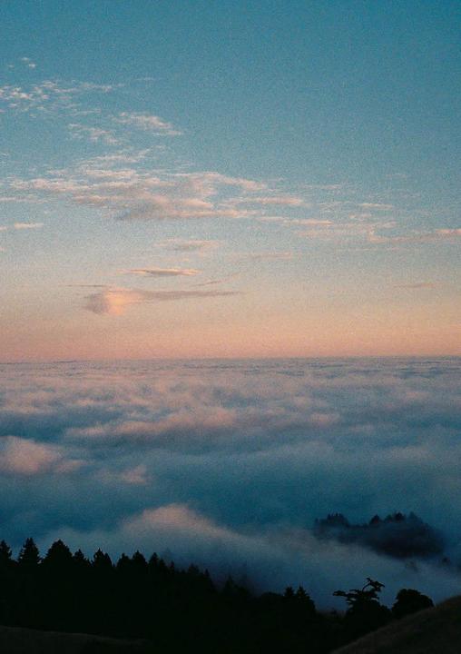 A layer of clouds stretches across the horizon with a line of trees visible below.