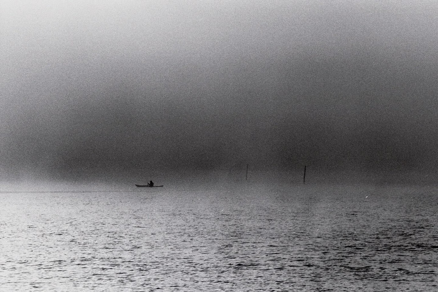 A person in a kayak is on the water in thick fog.
