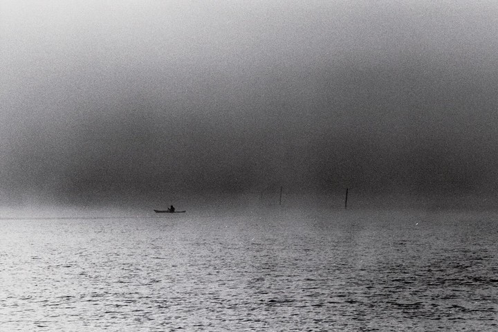 A person in a kayak is on the water in thick fog.