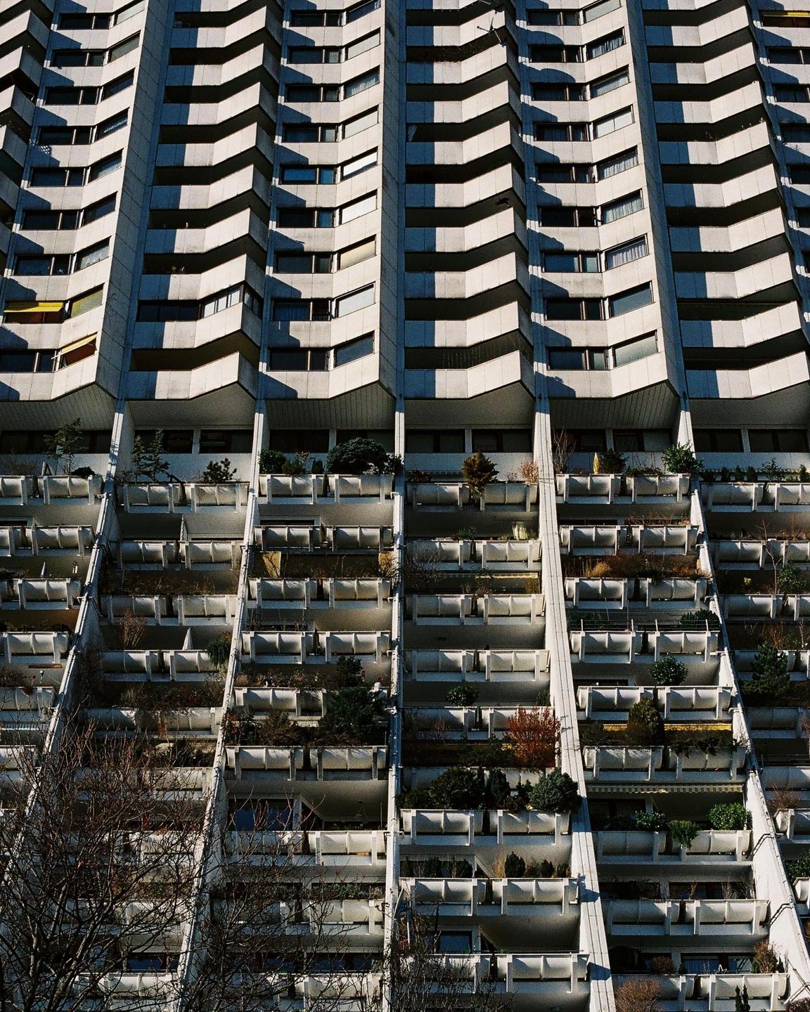 A tall building with many balconies and windows is shown from a low angle.