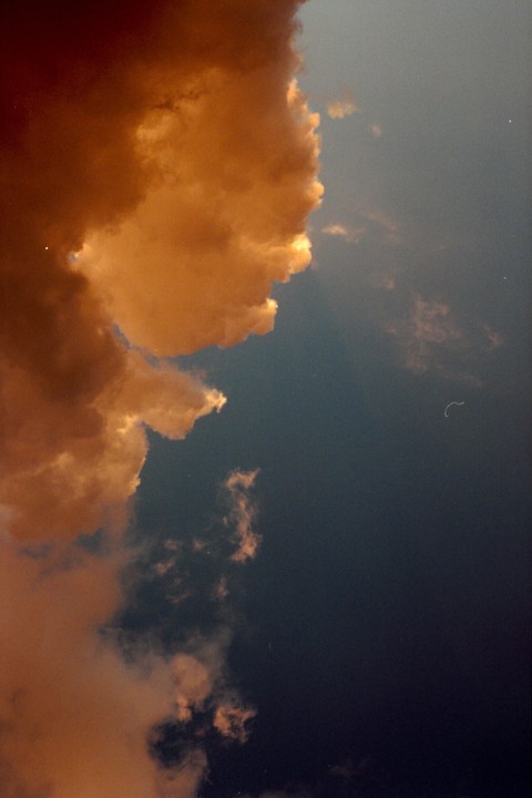 A large, brightly lit cloud fills the left side of the frame, contrasting with the dark blue sky on the right.