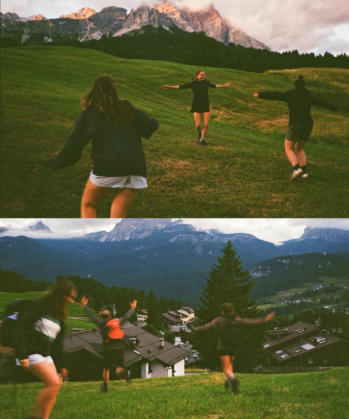 Three women run down a grassy hill with mountains in the background.