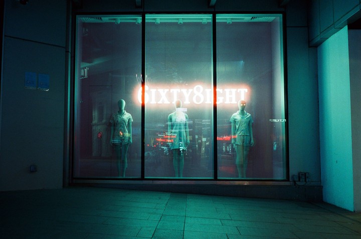 Three mannequins stand in a storefront window with a neon sign that reads "SIXTY8IGHT" above them.