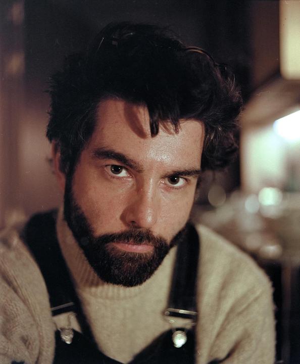 A man with a beard and dark hair looks directly at the viewer.