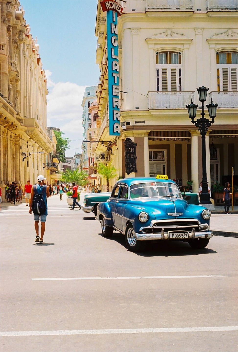 A blue vintage taxi is parked on a street in front of a building with a large "Hotel Inglaterra" sign.