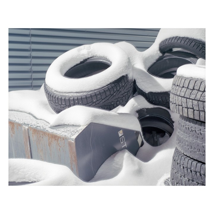 A pile of snow-covered tires sits next to a building.