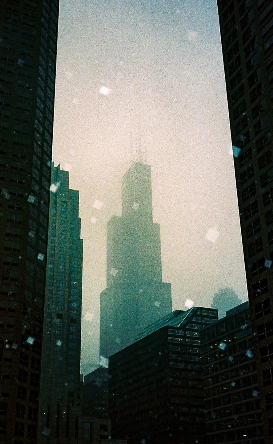 A tall skyscraper is visible through a gap between two other buildings on a snowy day.