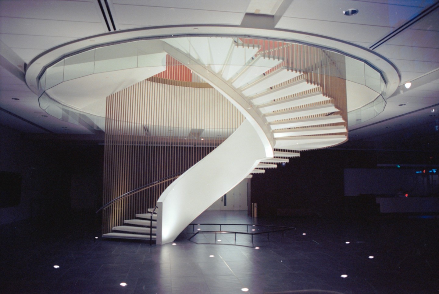 A modern spiral staircase with white steps and a glass railing ascends from a dark tiled floor.