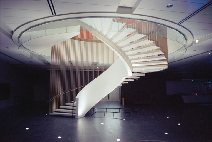 A modern spiral staircase with white steps and a glass railing ascends from a dark tiled floor.