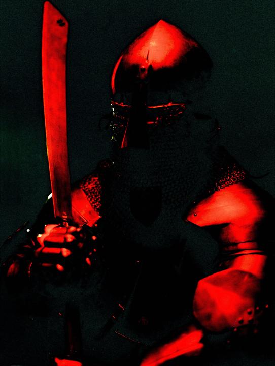 A knight in armor holds a sword, illuminated by red light.