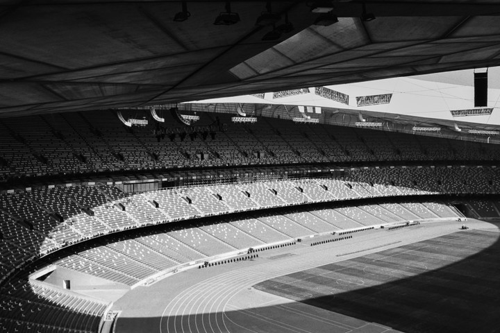 Sunlight illuminates a stadium track and rows of empty seats.