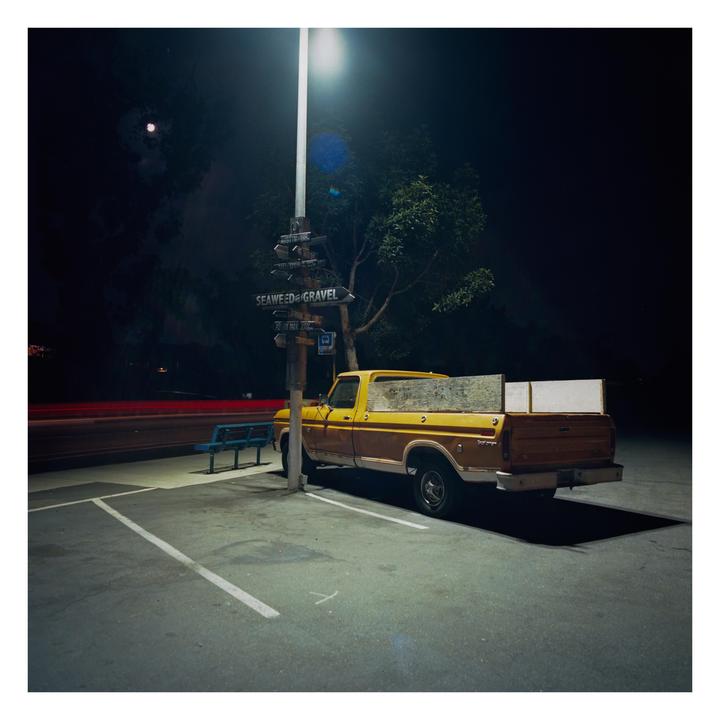 A yellow and brown pickup truck is parked under a street light at night, with a full moon visible in the sky.