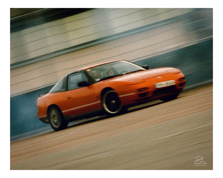An orange car drifts on a track, leaving a trail of smoke.