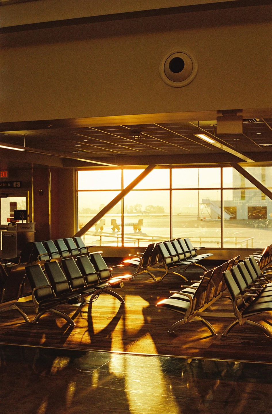 Empty airport gate seating is illuminated by golden hour light streaming through a large window overlooking the tarmac.