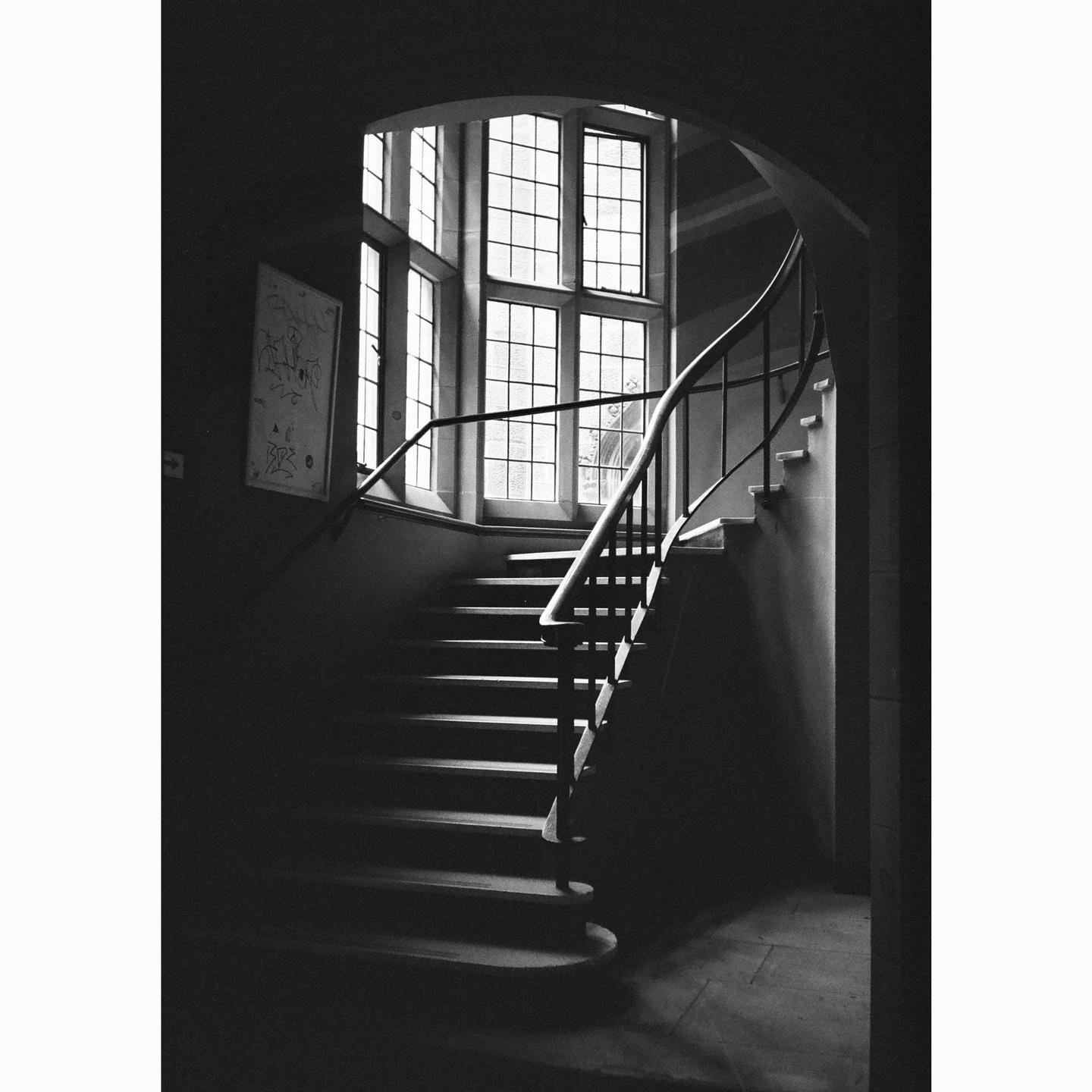 A grand staircase with a curved railing leads up to a large window with many panes.