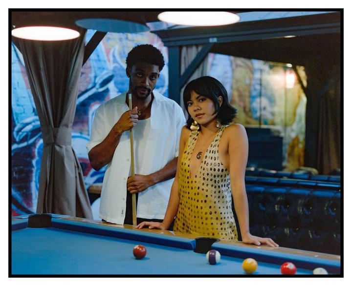 A man and a woman stand next to a pool table with billiard balls on it.