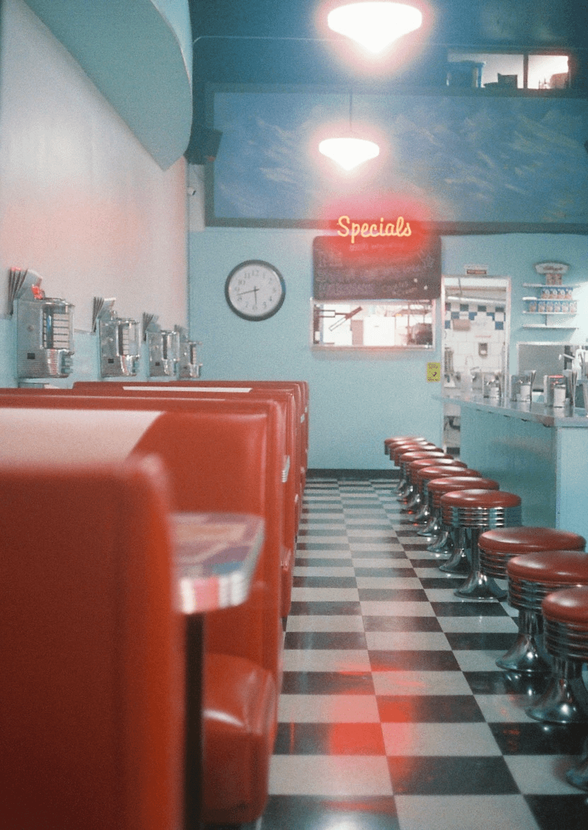 A diner interior features red booths and stools, a checkered floor, and a "Specials" neon sign.