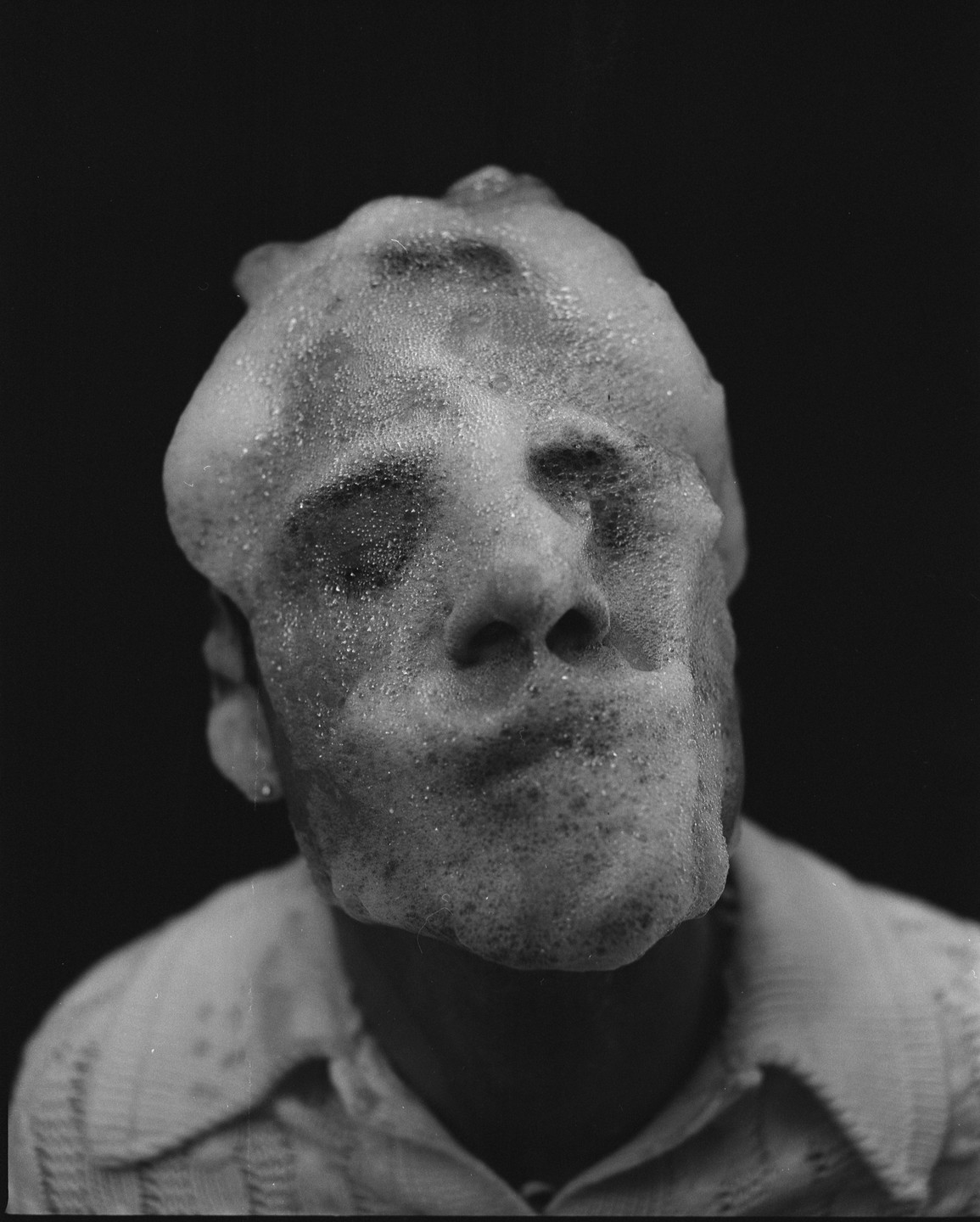 A man's face is covered in foam, with only his nose and mouth clearly visible.