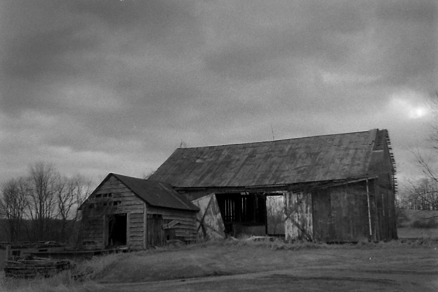 An old wooden barn with a smaller shed attached stands under a cloudy sky.