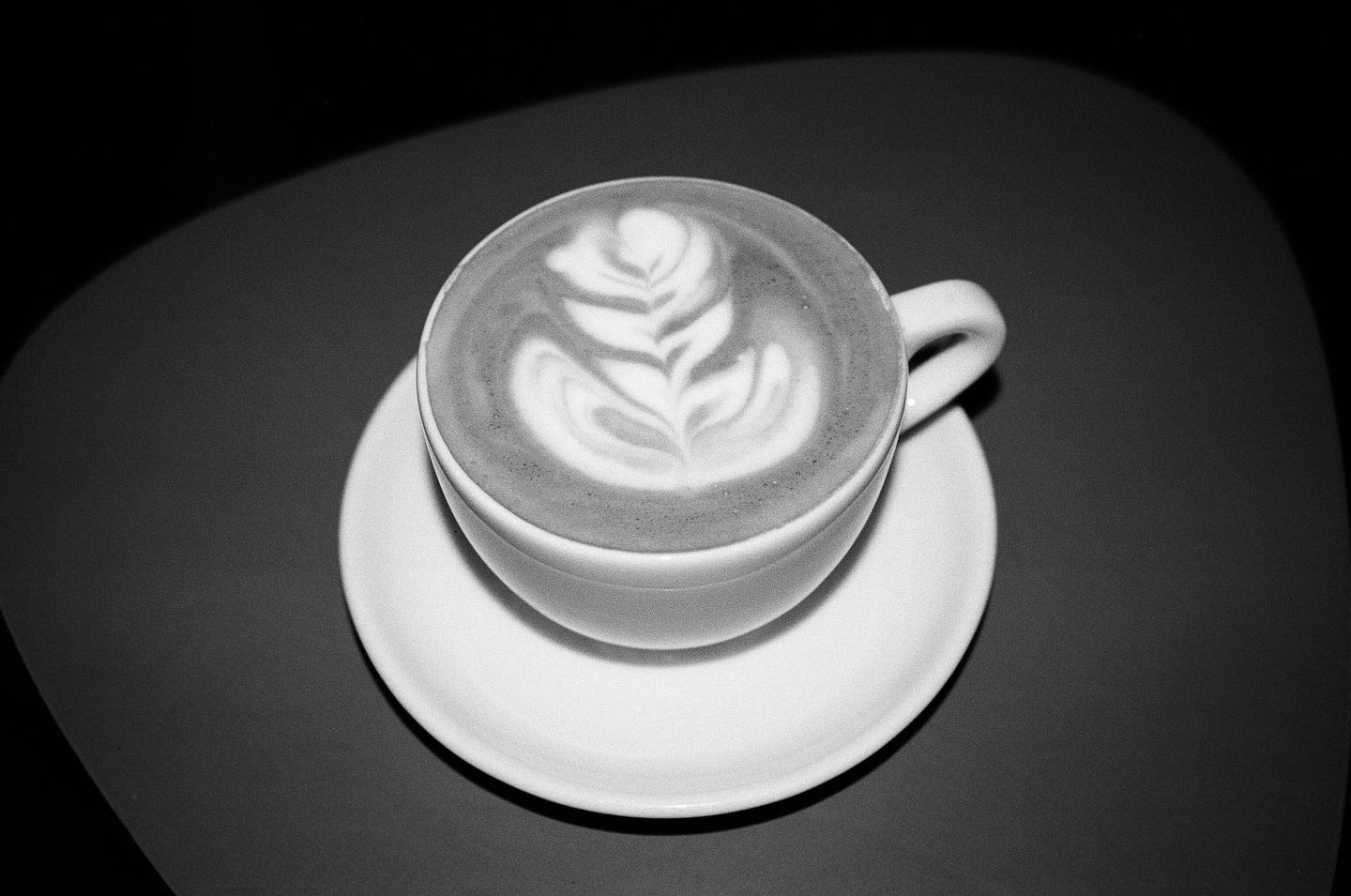 A cup of coffee with latte art sits on a saucer on a dark surface.