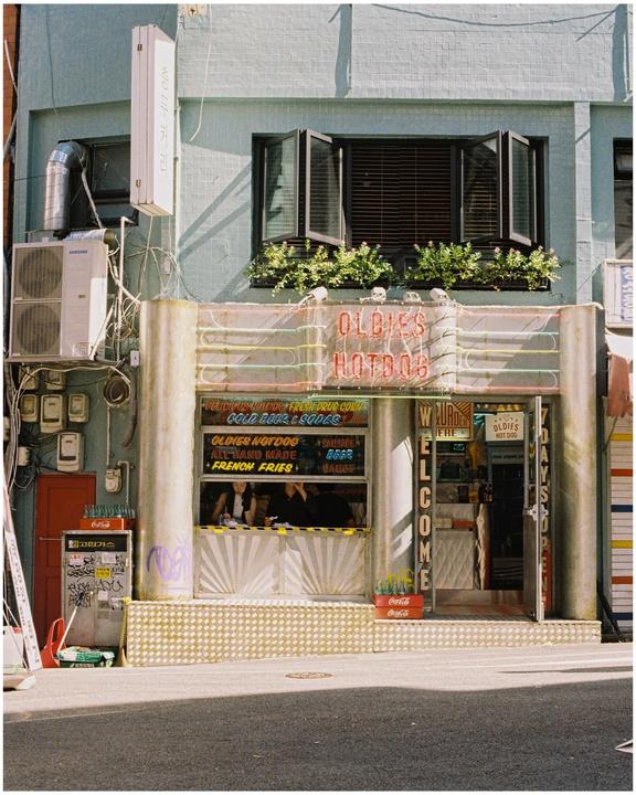 The storefront of Oldies Hotdog is visible from the street, with a woman sitting inside.
