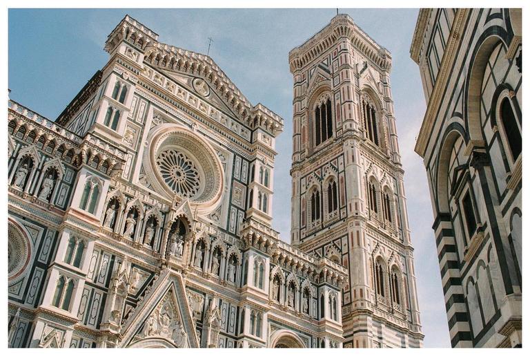 The facade of a large ornate cathedral with a tall bell tower next to it is viewed from below.