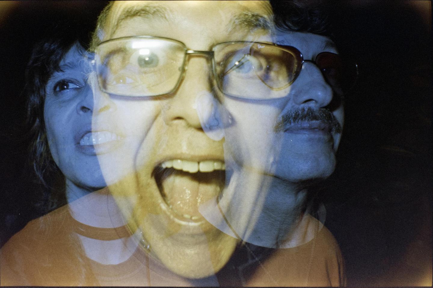 Three faces are visible in a multiple exposure, with one man in glasses screaming in the center.