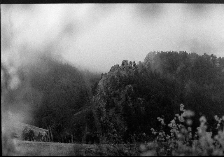 A black and white landscape shows a rocky, forested mountain shrouded in fog.