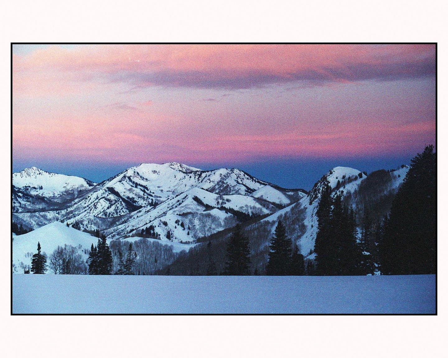 Snow-covered mountains and trees are visible under a pink and purple sky.