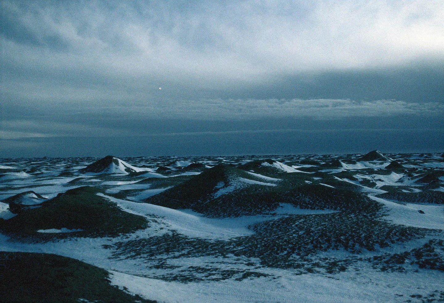 A vast, snow-covered landscape with rolling hills under a cloudy sky.