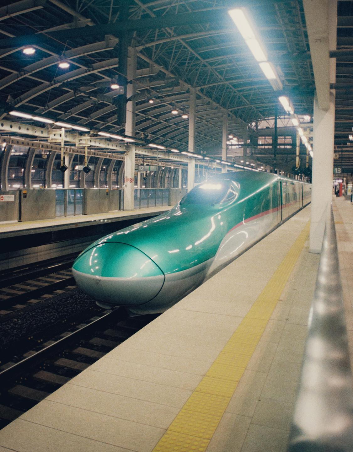 A green and white bullet train is stopped at a station platform under bright lights.