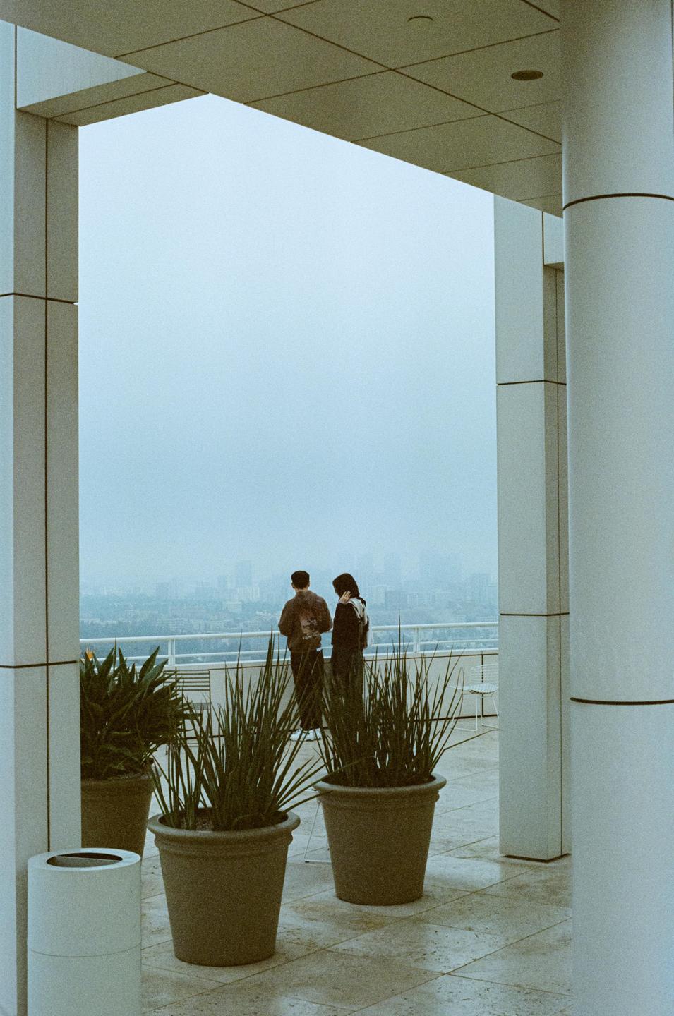A couple stands on a balcony overlooking a hazy city.