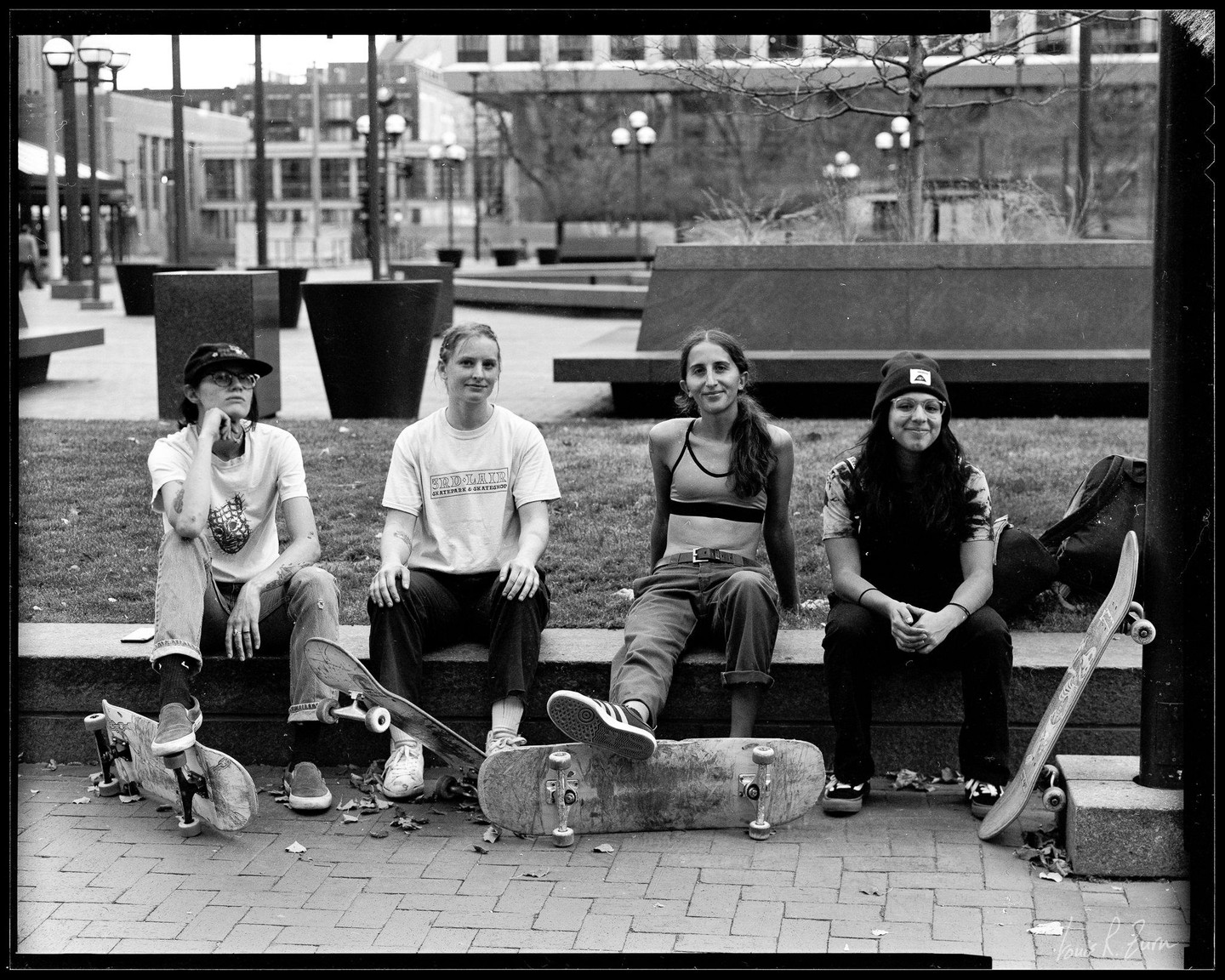 Four women sit on a ledge with skateboards around them.